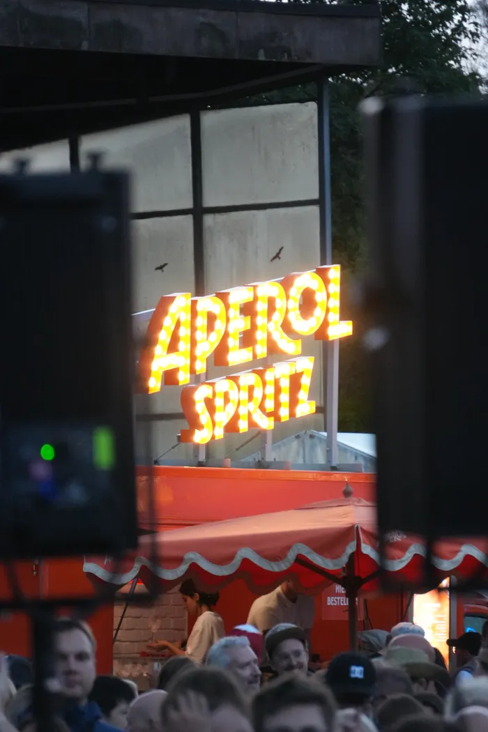 Ein leuchtendes Aperol Spritz Schild im Marquee-Stil über einem roten Zelt und einer Menschenmenge.