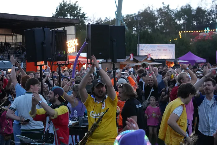 Musiker der Band Knallblech spielen mit Blasinstrumenten inmitten einer Menschenmenge bei einem Open-Air-Festival.
