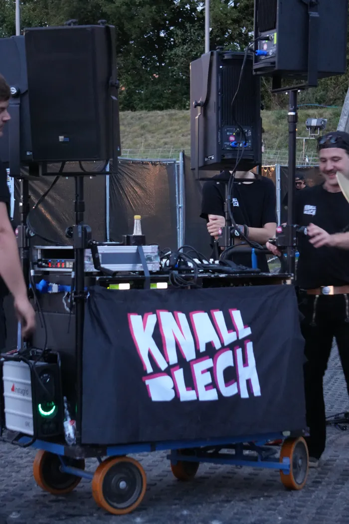 Mobiler DJ-Wagen mit großen Lautsprechern und einem schwarzen Banner mit dem pink-weißen Schriftzug „KNALL BLECH“.