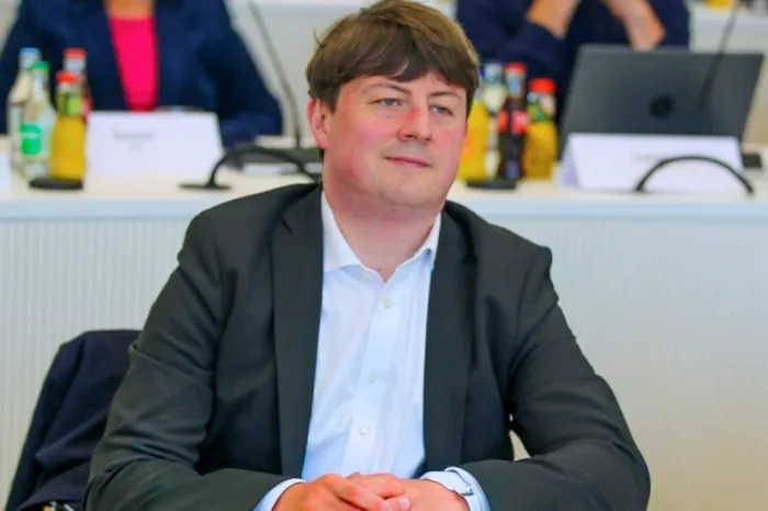 Fabian Ferber sitzt in einem dunklen Sakko und weißem Hemd mit verschränkten Händen an einem Tisch.