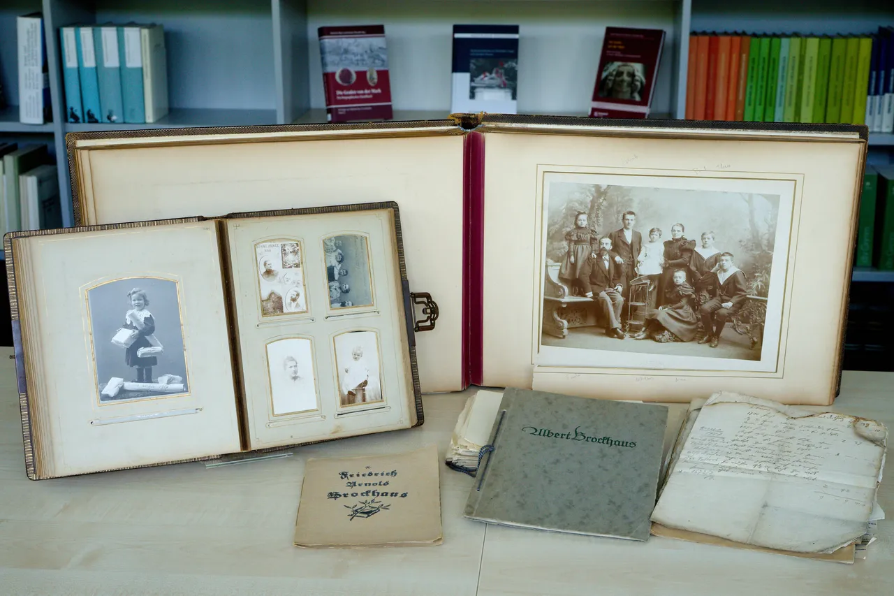 Offener Fotoalbum mit historischen Schwarzweißfotos einer Familie und darunter Briefe und Dokumente mit dem Namen „Brockhaus“.