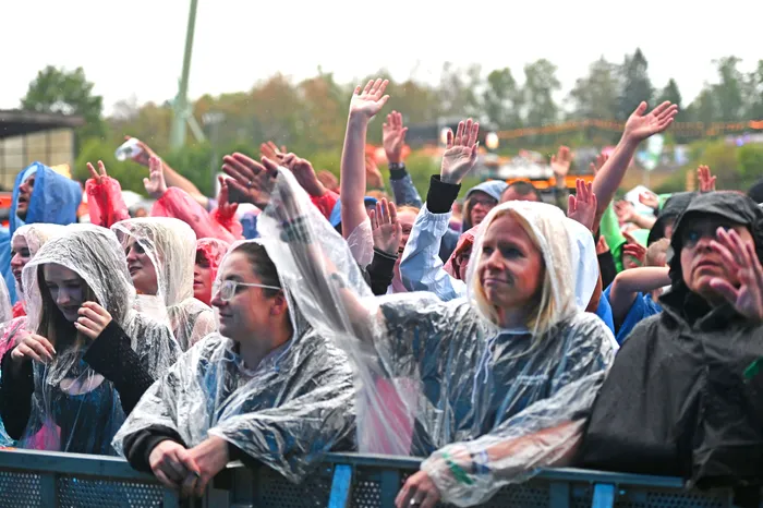 Eine Menschenmenge in Regenponchos mit erhobenen Händen bei einem Open-Air-Event.