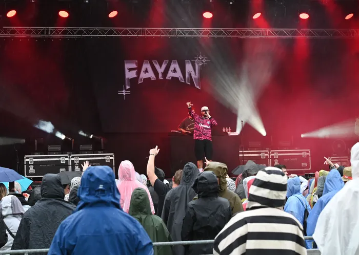 Fayan performt auf einer Bühne mit roter Beleuchtung und großem Schriftzug vor einer Menge von Zuschauern in Regenbekleidung.