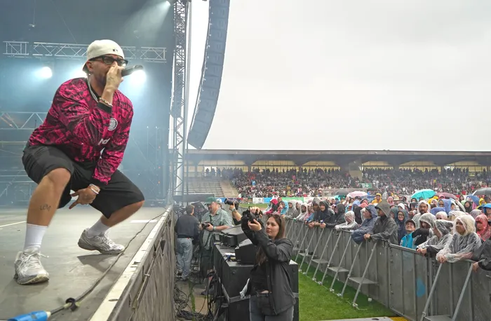 Der Sänger Fayan singt in ein Mikrofon auf einer Bühne vor einer großen Menschenmenge bei einem Open-Air-Konzert.