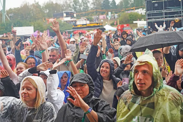 Eine Menschenmenge von Fans bei einem Open-Air-Event hebt die Hände in die Luft, viele tragen Regenbekleidung.