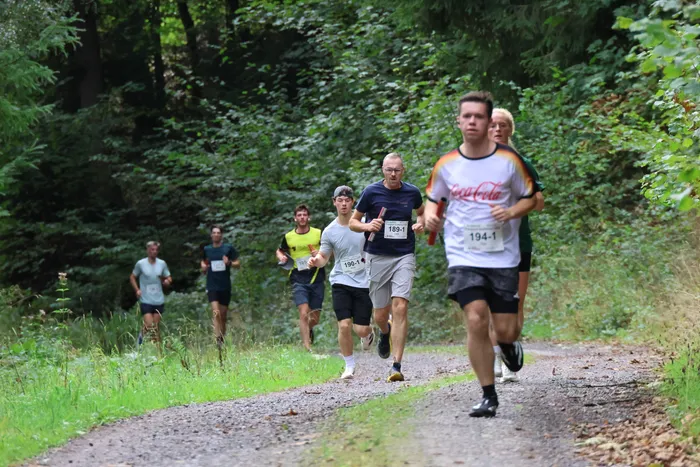 Mehrere Läufer nehmen an einem Staffellauf auf einem Schotterweg durch einen Wald teil.