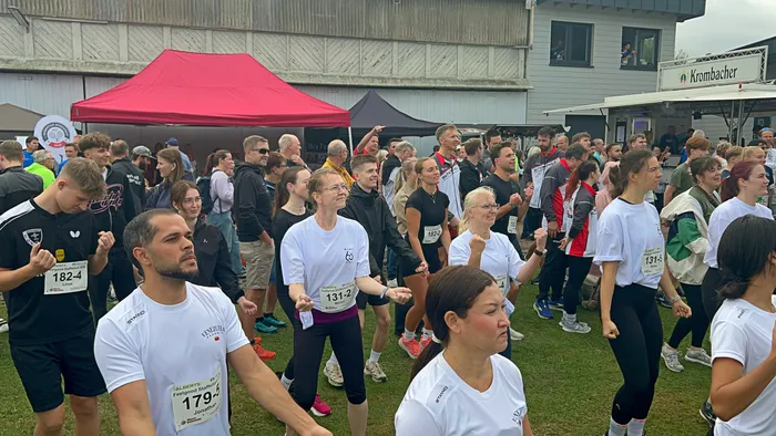 Teilnehmer des Feelgood-Staffellaufs stehen auf einer Wiese vor einem roten Zelt; viele tragen weiße T-Shirts mit Startnummern.