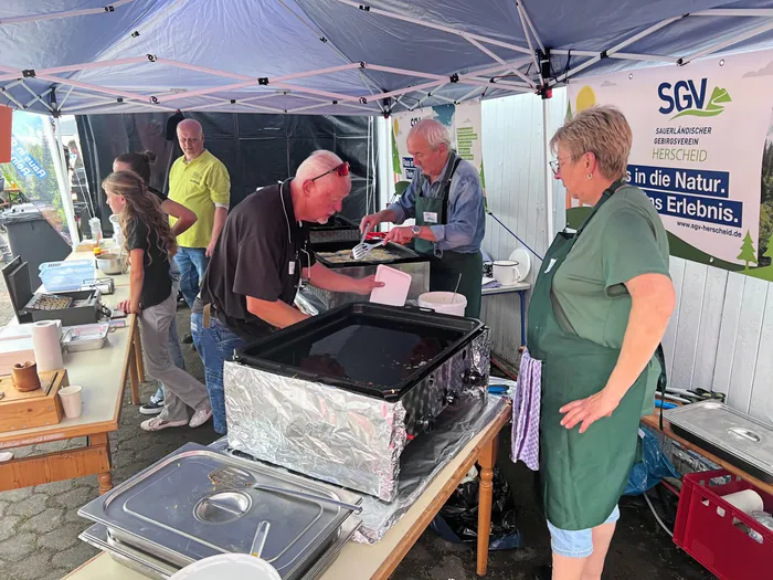 Menschen bereiten an einem Stand unter einem blauen Zelt Speisen auf einer Grillplatte zu.