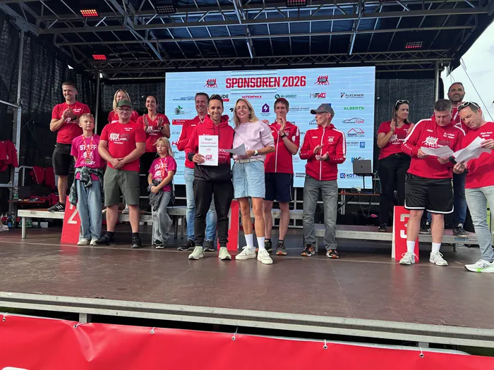 Ein Mann und eine Frau halten auf einer Bühne beim Feelgood-Staffellauf 2026 eine Urkunde vor einer Sponsorenwand hoch.