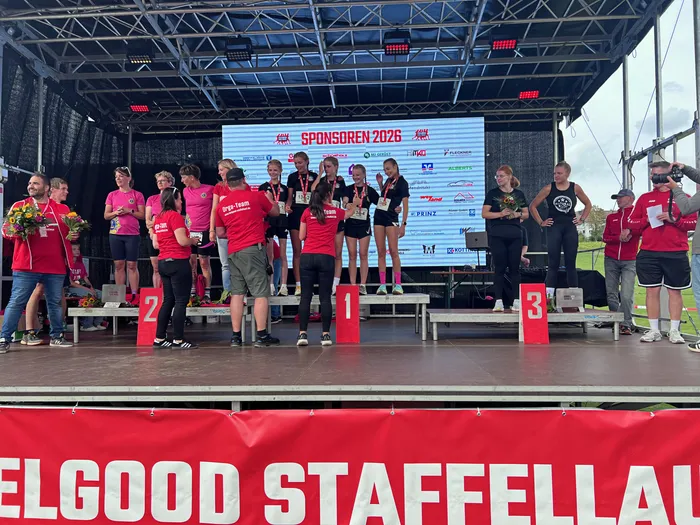 Siegerehrung beim Feelgood-Staffellauf auf einer Bühne mit einem Podium und einer Sponsorenwand im Hintergrund.