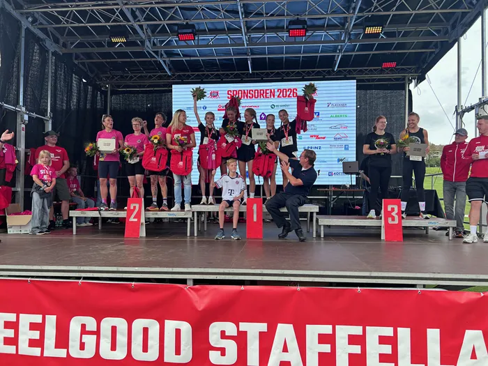Siegerinnen des Feelgood-Staffellaufs stehen auf einem Podium und halten Blumen sowie Trophäen hoch.