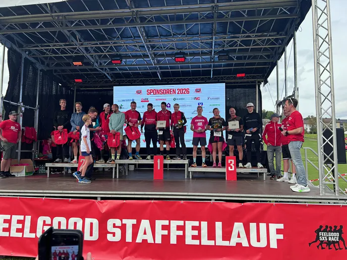 Teilnehmer halten Trophäen auf einer Bühne beim Feelgood-Staffellauf vor einer Sponsorenwand.