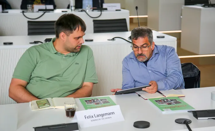Felix Langemann und Paolino Barone sitzen an einem Tisch; Barone blickt auf ein Tablet.