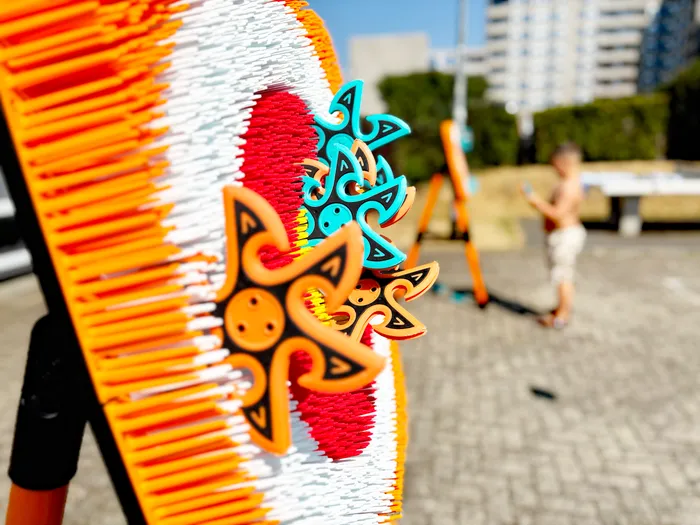 Nahaufnahme eines farbenfrohen Objekts mit orangefarbenen, weißen und roten Kunststoffborsten und sternförmigen Elementen in Blau und Orange.
