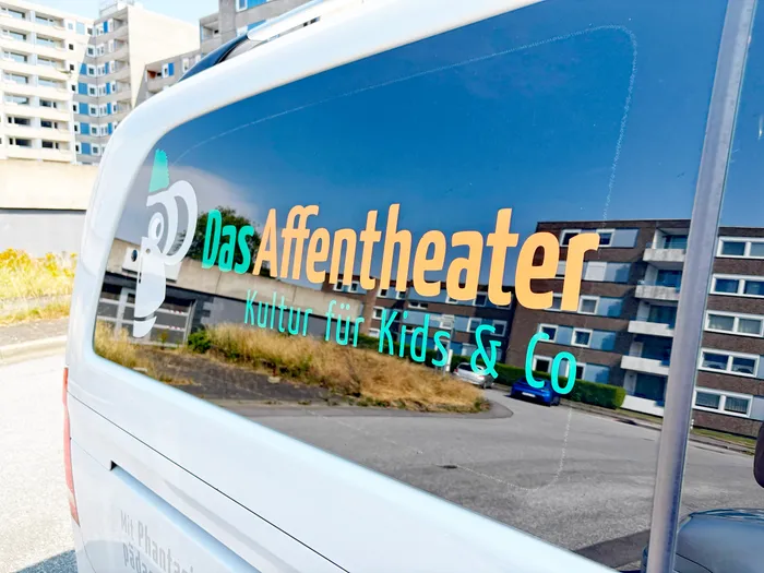 Logo und Schriftzug „Das Affentheater – Kultur für Kids & Co“ auf der Fensterscheibe eines weißen Transporters.