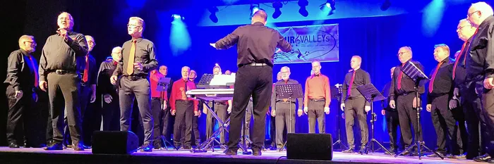 Das A-cappella-Ensemble LaLeLu singt auf einer Bühne unter blauem und rotem Licht, geleitet von einem Dirigenten.