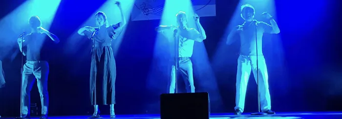 Vier Mitglieder des A-cappella-Ensembles LaLeLu performen mit Mikrofonen auf einer Bühne unter blauem Scheinwerferlicht.
