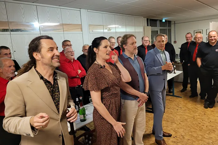 Mitglieder des A-cappella-Ensembles LaLeLu und weitere Personen stehen in einer Gruppe in einem hellen Raum.