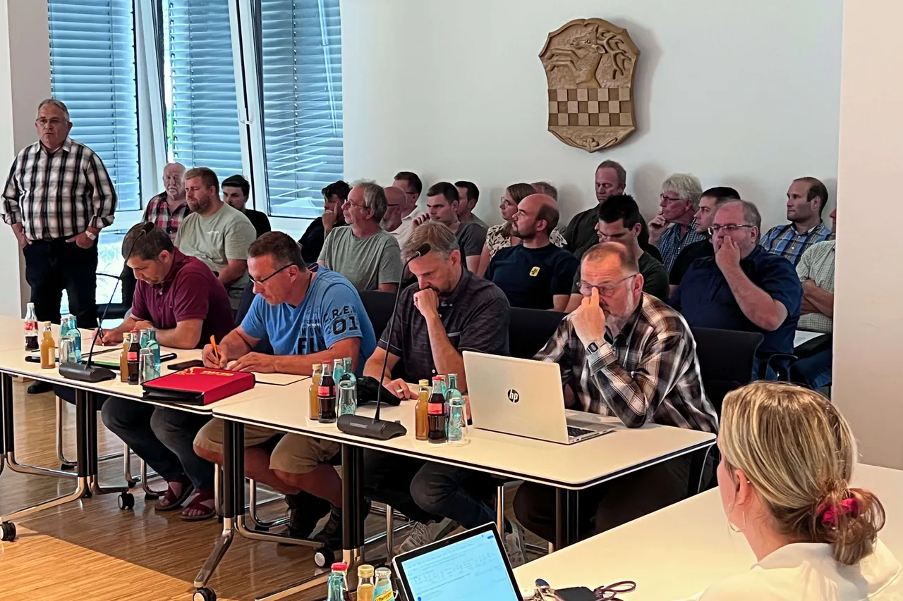 Zahlreiche Männer sitzen an Tischen in einem hellen Raum und verfolgen eine Diskussion. Im Hintergrund steht ein Mann und spricht.