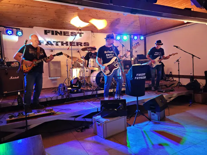Die Hardrockcoverband Finest Fathers spielt live auf einer Bühne mit Schlagzeug, Gitarren und bunten Scheinwerfern.