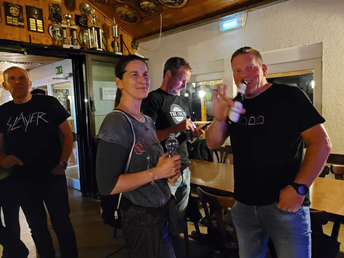 Eine Gruppe von Menschen steht in einem Raum mit Holzwänden und Trophäen; ein Mann hält eine Flasche hoch.