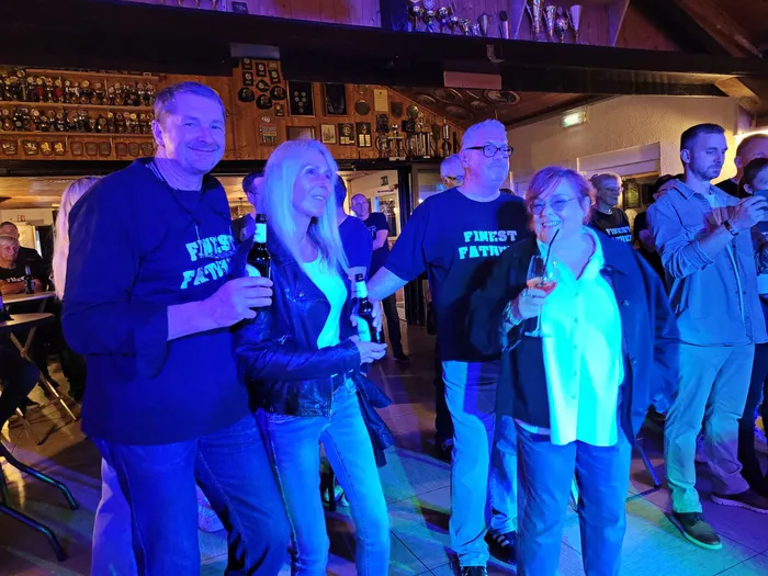 Eine Gruppe von Menschen feiert mit Getränken bei der Veranstaltung „Gipfelrock“, einige tragen Kleidung der Band Finest Fathers.