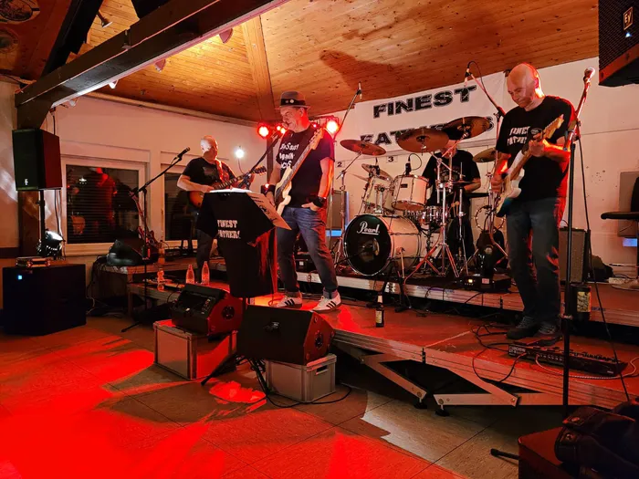 Die Hardrockcoverband Finest Fathers spielt live auf einer Bühne mit roter Beleuchtung vor einem Banner.