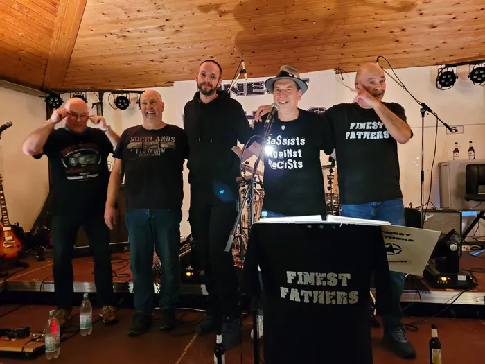 Die fünf Mitglieder der Hardrockcoverband Finest Fathers posieren lächelnd auf einer Bühne.