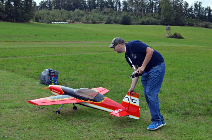 Ein Mann beugt sich über ein rot-gelbes Modellflugzeug, um es auf einer grünen Wiese vorzubereiten.