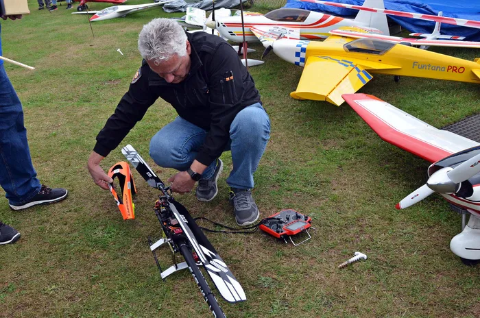 Ein Modellflugpilot kniet auf einer Wiese und arbeitet an einem schwarz-weißen Modellflugzeug. Im Hintergrund liegen weitere Flugmodelle.