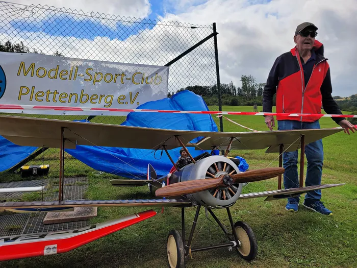 Ein Modell-Doppeldecker steht auf einer Wiese neben einem Mann vor einem Schild des Modell-Sport-Clubs Plettenberg e.V.