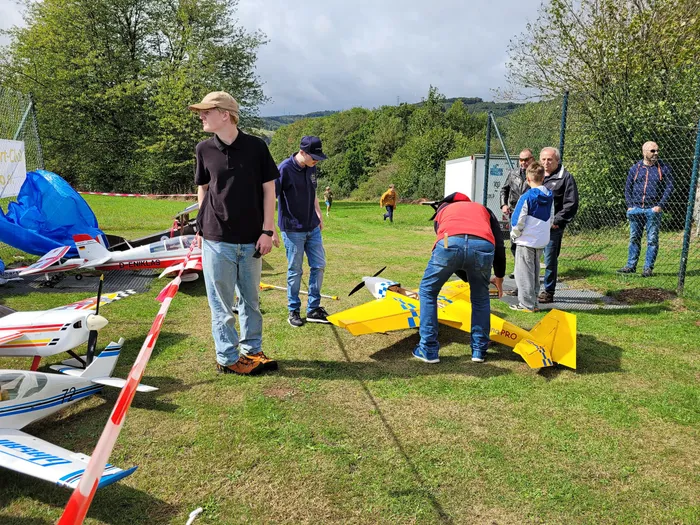 Modellflugpiloten bereiten auf einer Wiese ein großes gelbes Modellflugzeug vor, während weitere Modelle am Boden liegen.