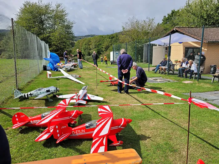 Rote und weiße Modellflugzeuge auf einer Wiese, umgeben von Personen bei einem Flugplatzfest.
