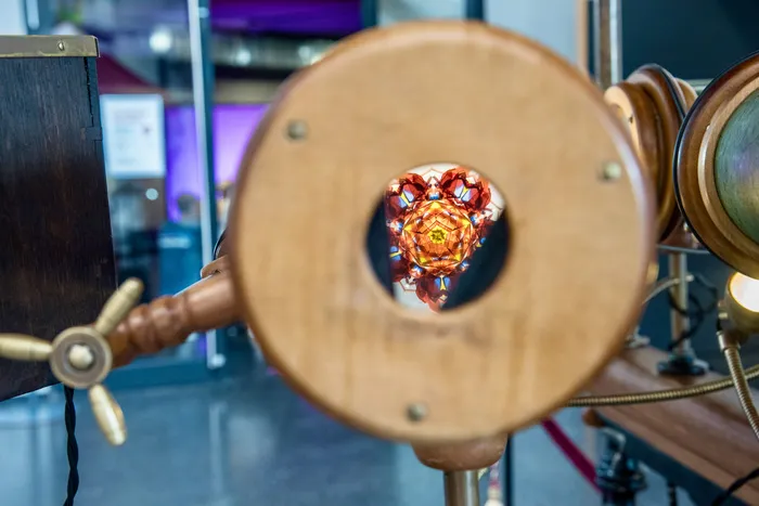 Blick durch eine kreisförmige Holzöffnung auf ein buntes, kaleidoskopisches Muster eines Exponats.