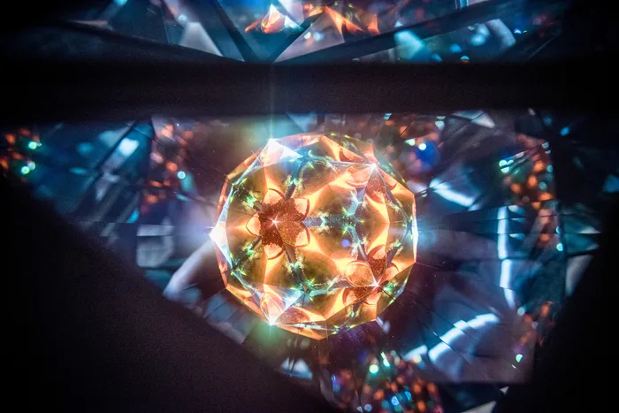 Eine leuchtende, facettenreiche Kugel mit orangefarbenen Lichtmustern vor einem dunklen, geometrischen Hintergrund.