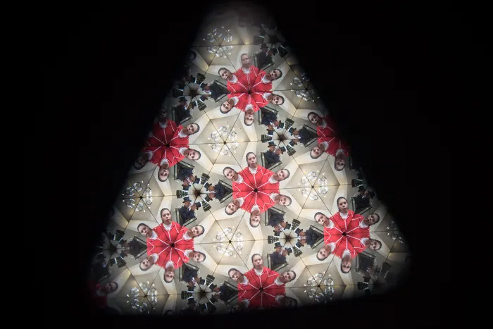 Kaleidoskopisches Muster mit sich wiederholenden Gesichtern und roten, sternförmigen Elementen.