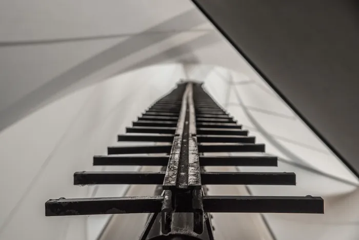 Blick von unten auf eine dunkle Metallkonstruktion, die steil in einen hellen, gewölbten Raum ragt.