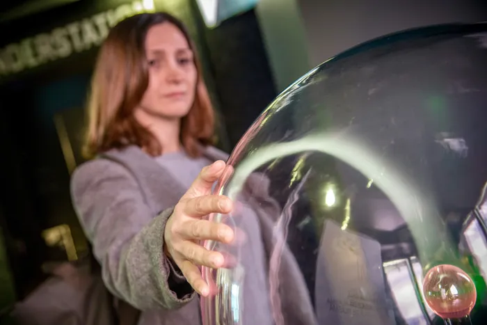 Eine Frau berührt eine große, transparente, gewölbte Glasinstallation im Erlebnismuseum Phänomenta.