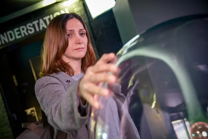 Eine Frau in einem grauen Mantel berührt ein großes, transparentes Exponat im Museum Phänomenta.