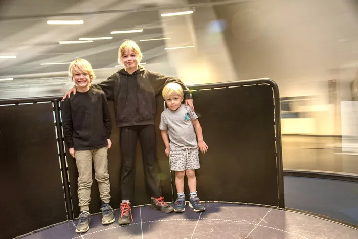 Drei lächelnde Jungen stehen nebeneinander vor einer dunklen Wand im Erlebnismuseum Phänomenta.