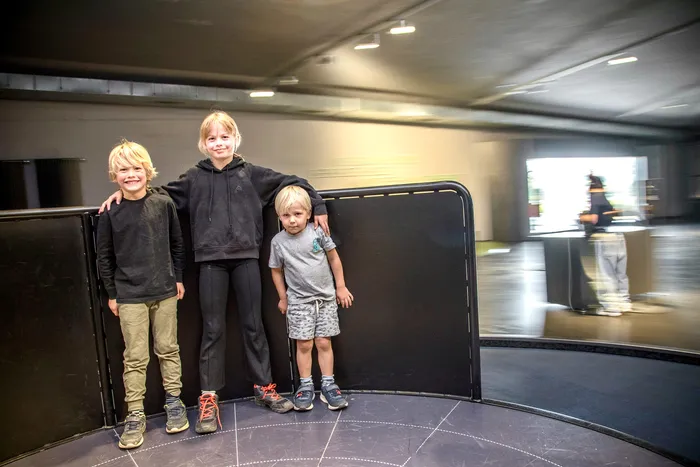 Drei lächelnde Jungen stehen nebeneinander in einem Raum des Erlebnismuseums Phänomenta.