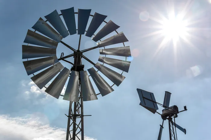 Zwei metallene Windräder vor einem strahlend blauen Himmel mit einer hellen Sonne.