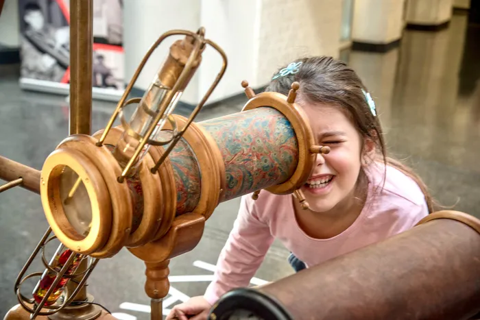 Ein lachendes Mädchen blickt durch ein großes, gemustertes wissenschaftliches Instrument im Museum Phänomenta.