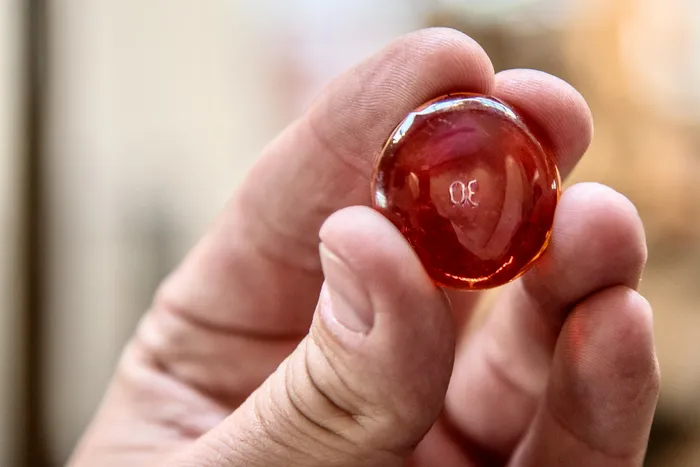 Eine Hand hält ein kleines, rötlich-transparentes Glasobjekt mit der eingravierten Zahl 30.