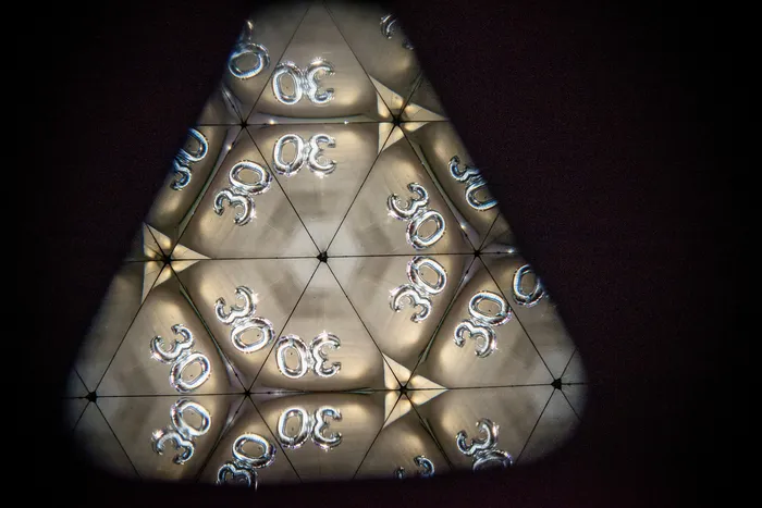 Kaleidoskopische Darstellung der Zahl 30 in einem geometrischen Muster vor dunklem Hintergrund.