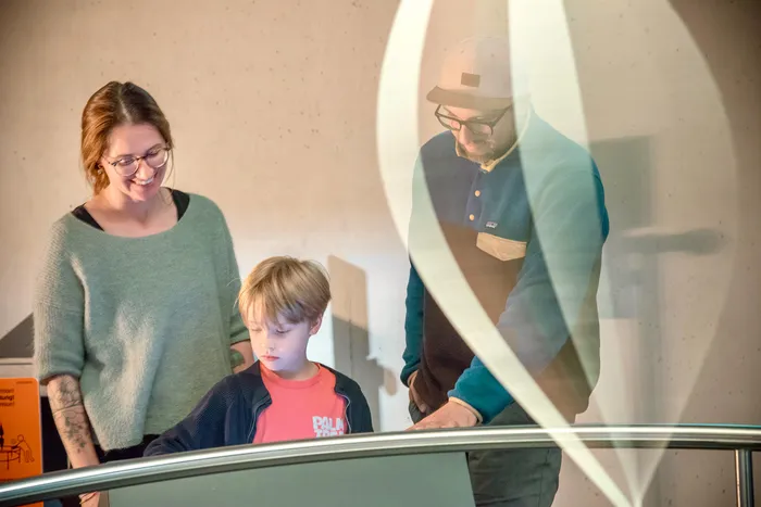 Eine Frau, ein Junge und ein Mann blicken gemeinsam auf ein Exponat im Erlebnismuseum Phänomenta.