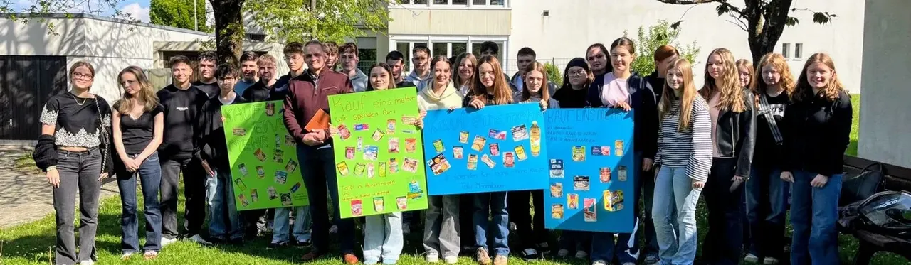 Eine Gruppe Jugendlicher hält Plakate mit Abbildungen von Lebensmitteln, um für Spenden an die Tafel zu werben.