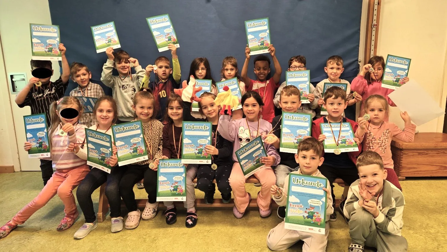 Eine Gruppe von Kindern hält Urkunden und Medaillen hoch in die Kamera. Sie haben das Bewegungsabzeichen „Benni und Frida“ erhalten.