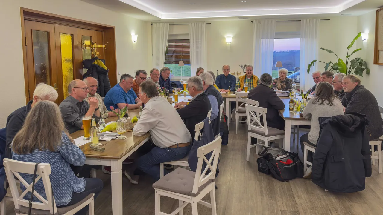 Versammlung des Bürgerbusvereins mit rund 20 Personen an einem langen Tisch, einige unterhalten sich, andere essen oder trinken.