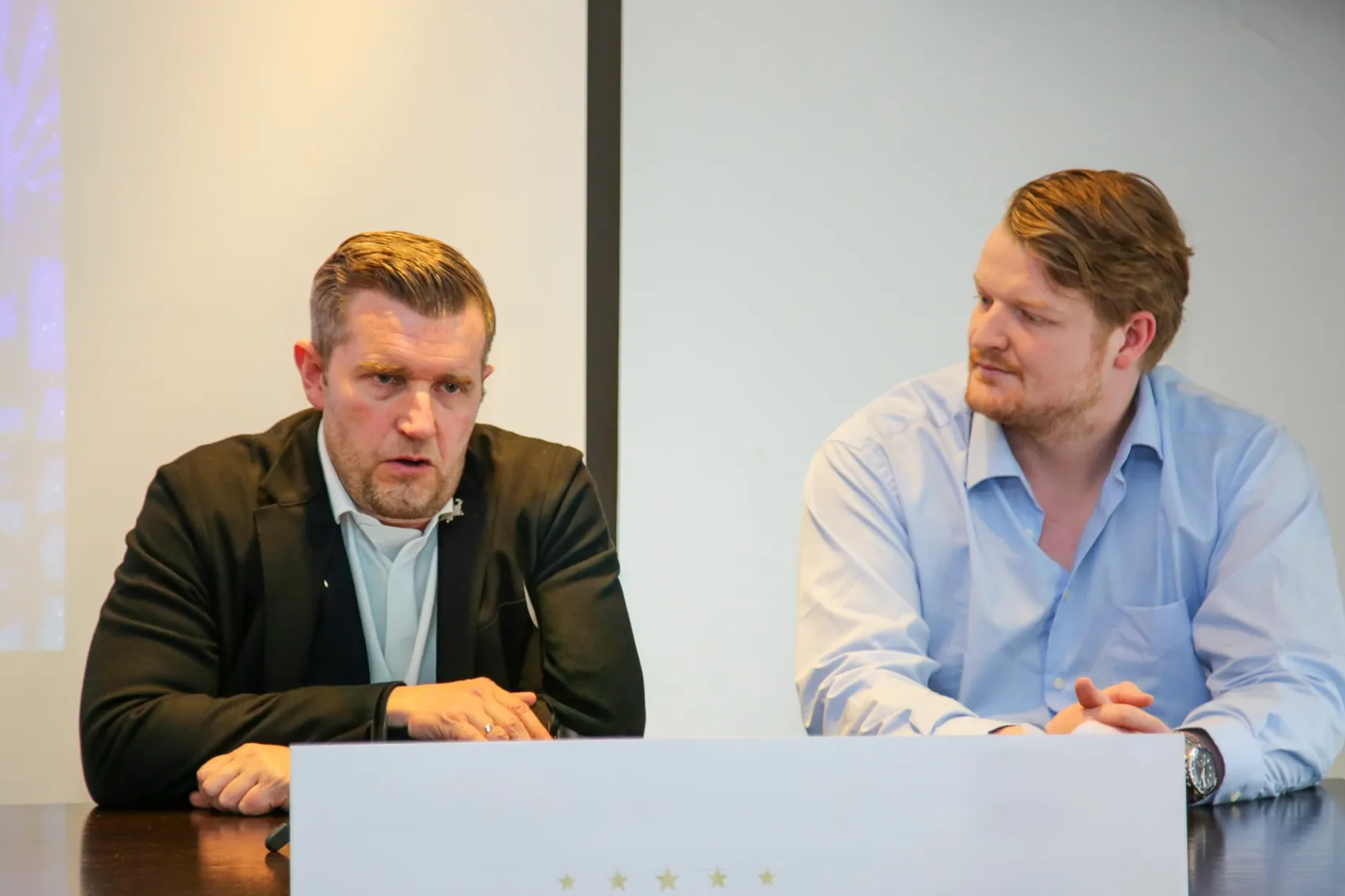 Franz-David Fritzmeier, Sportdirektor der Roosters, und Pressesprecher Felix Dötsch sitzen an einem Tisch und sprechen während einer Saisonbilanz.